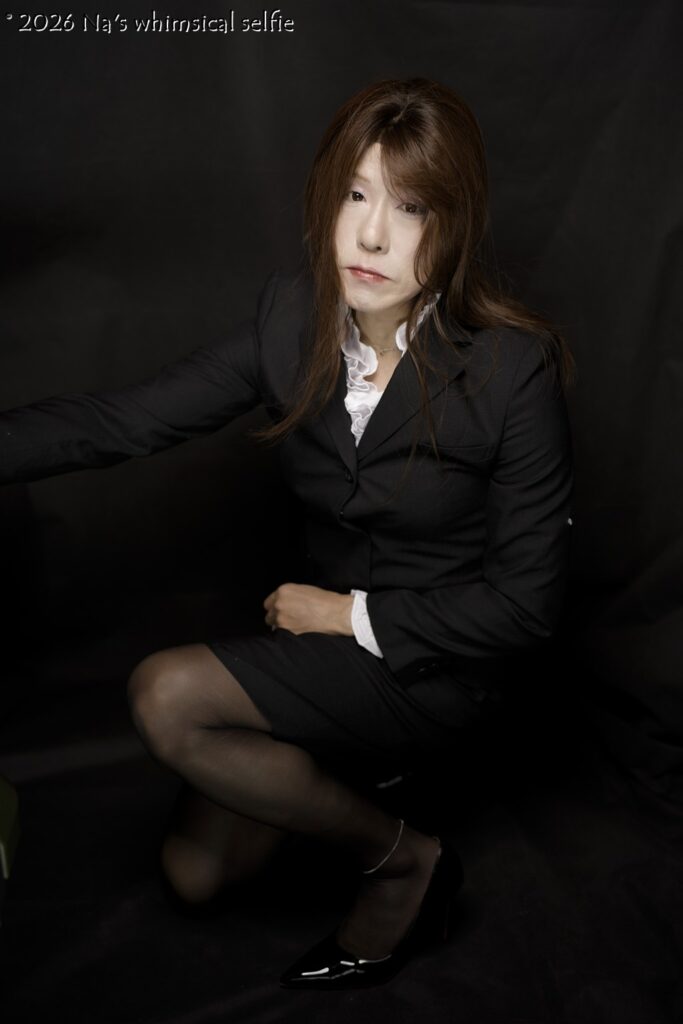 黒背景の前で黒いスーツを着て、静かな表情で座るNaのセルフポートレート SONY α1 + SONY Planar T* FE 50mm F1.4 ZA